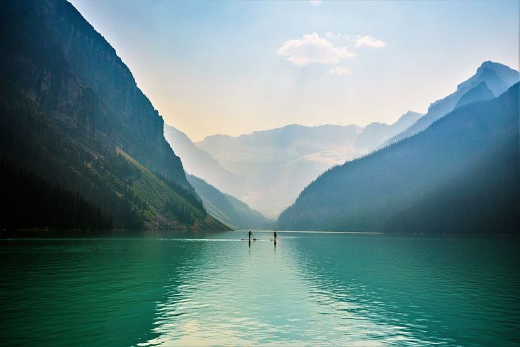 People paddleboarding in lake against mountains and sky