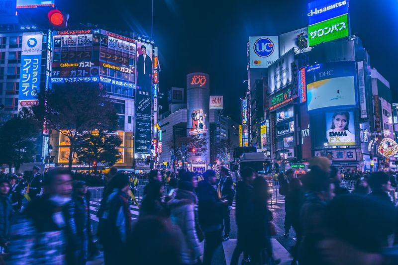 People on illuminated street amidst buildings in city at night in shibuya tokyo japan