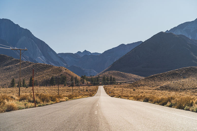 Empty road leading towards mountains against clear sky
