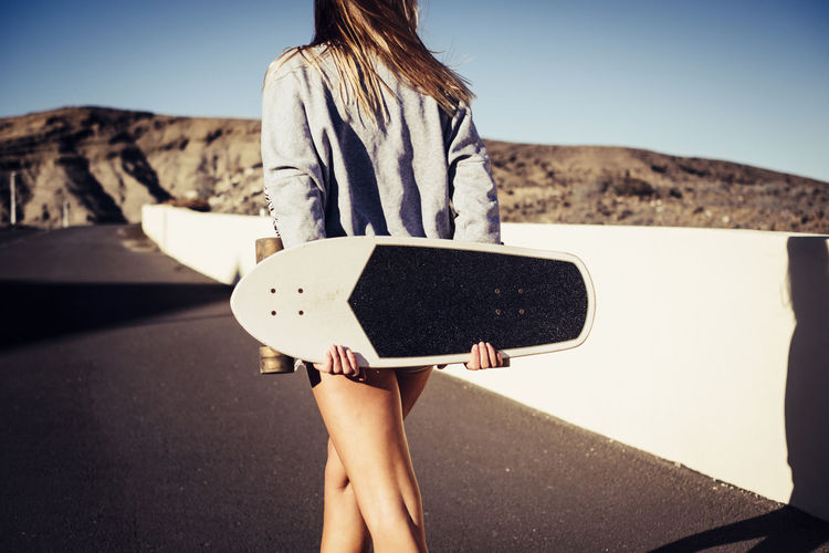Rear view of woman holding skateboard while walking on road