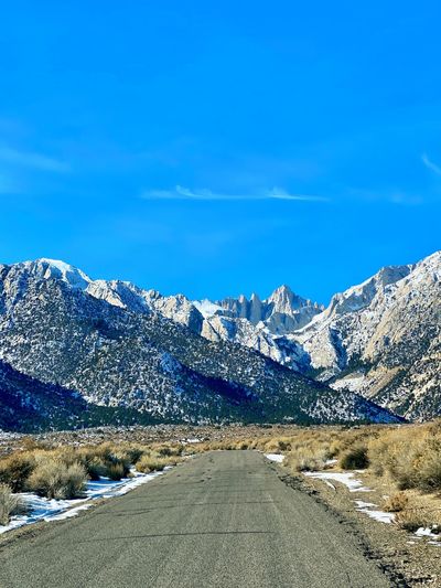 Road amidst snowcapped mountains against blue sky