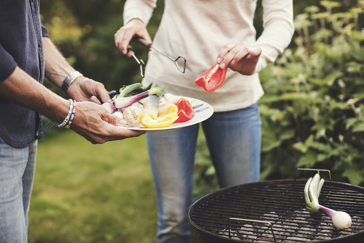 Midsection of father and daughter cooking vegetables on barbecue grill in back yard