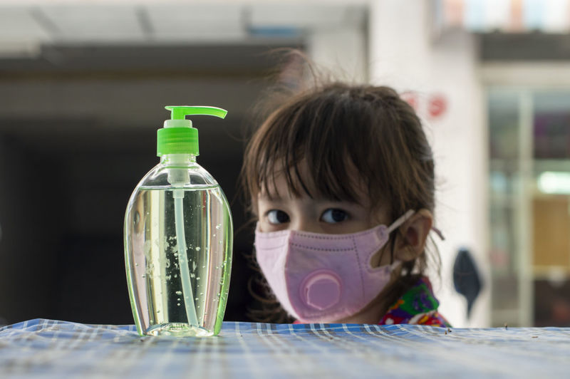 Portrait of cute girl wearing mask by hand sanitizer