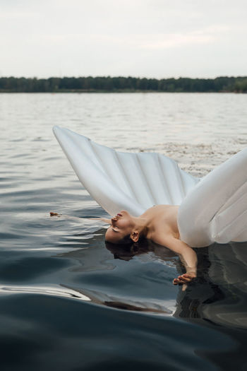 Shirtless woman floating with inflatable raft on lake against sky