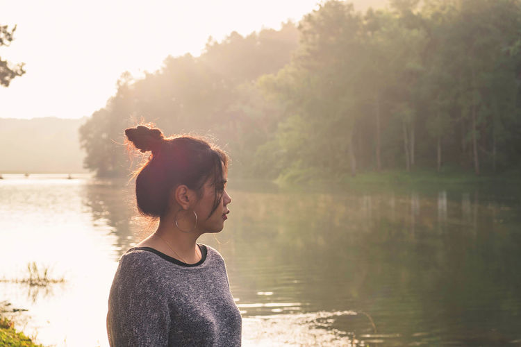 Woman standing by lake against trees