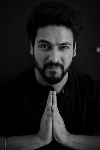 Portrait of young man gesturing while standing against black background