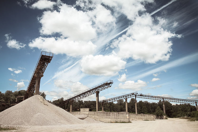 Low angle view of conveyor belt on sand pile at mine against sky