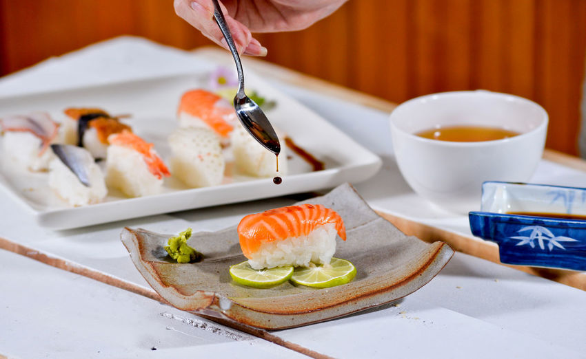 Cropped image of hand pouring sauce over sushi on table