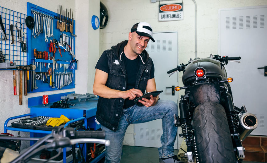 Portrait of man leaning by motorcycle in garage