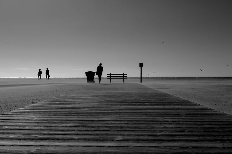 People on pier at beach against clear sky