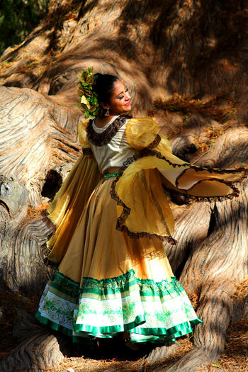 Young woman in traditional clothing dancing against large tree