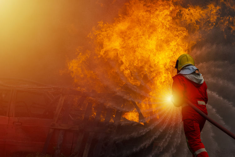 A firefighter in suit and helmet is extinguishing that the fire is burning, copy space.