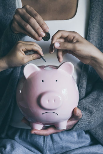 Close-up hands putting coin in unhappy sad piggy bank. people saving money for household payments.