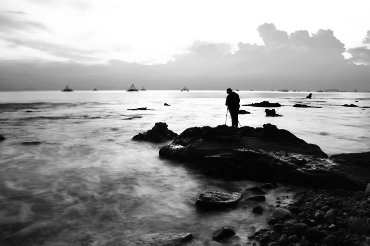 Silhouette man standing on rock against sea at beach