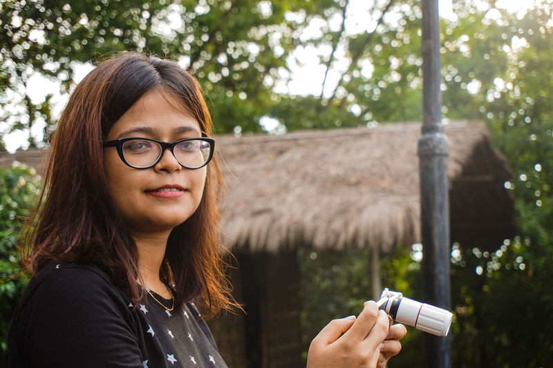 Portrait of smiling woman with smart phone standing against hut