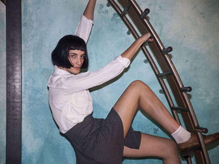 Portrait of woman climbing ladder against wall