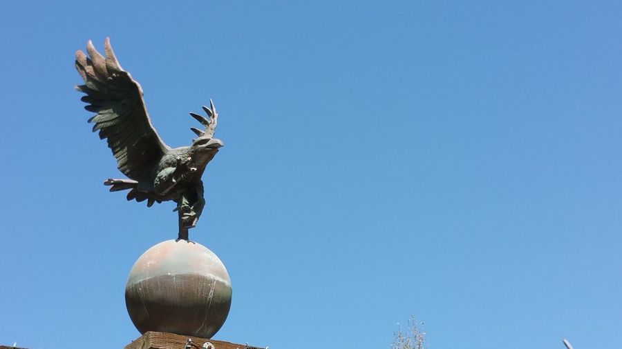 Low angle view of eagle statue flying against clear blue sky