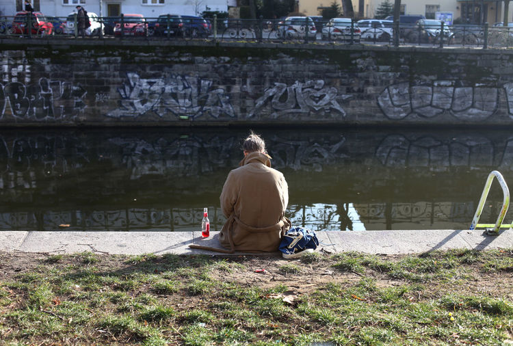 Rear view of woman sitting by canal with reflection