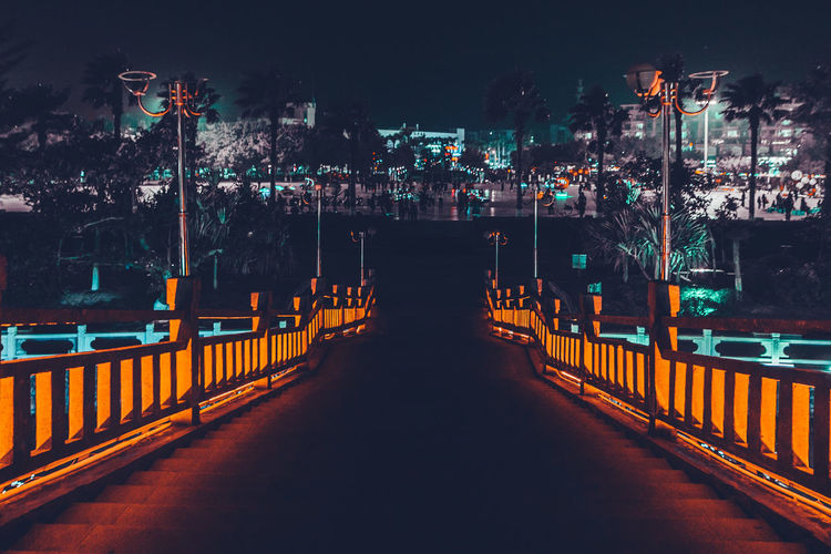 Illuminated street lights by bridge in city at night