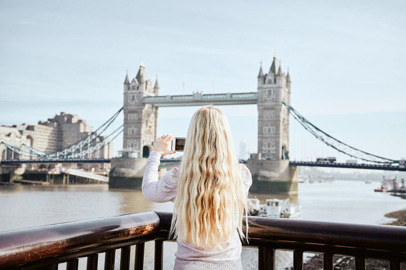Blonde woman with wavy hair taking picture of tower bridge