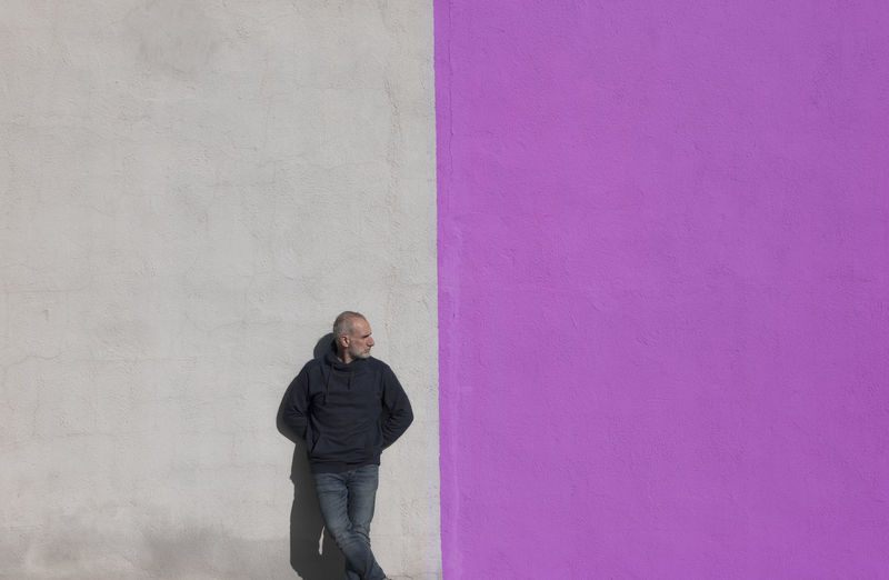 Adult man standing against white and purple wall