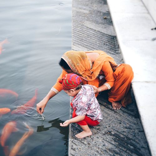 High angle view of mother and son looking at koi carps in lake