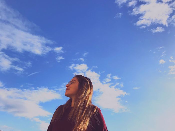 Low angle view of young woman against blue sky