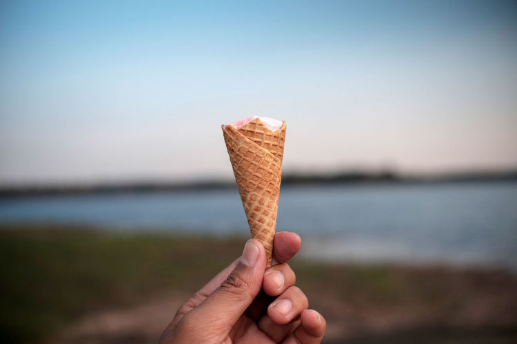 Hand holding ice cream against sky