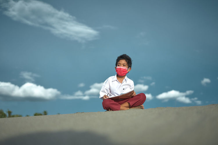 Portrait of boy sitting on land against sky