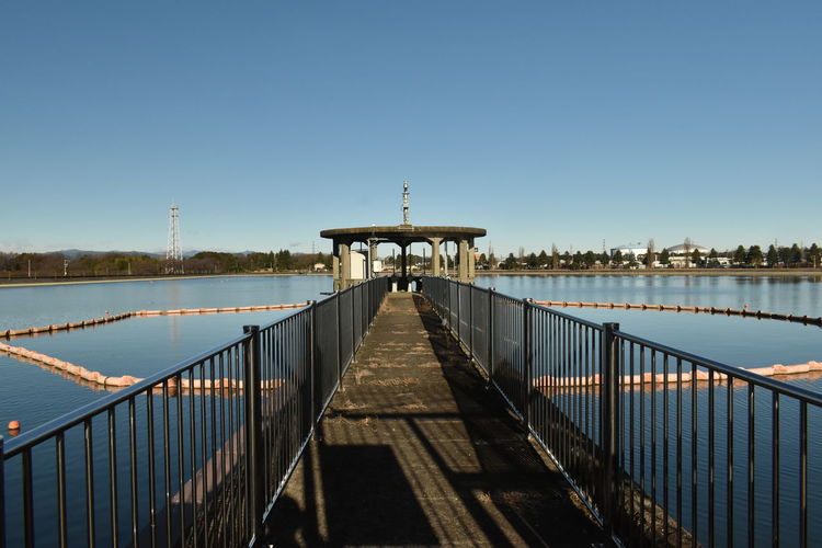 Pier on footbridge against clear blue sky