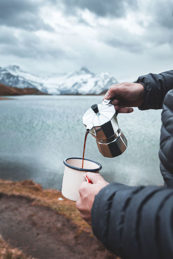 Cropped image of hand holding coffee cup against sea