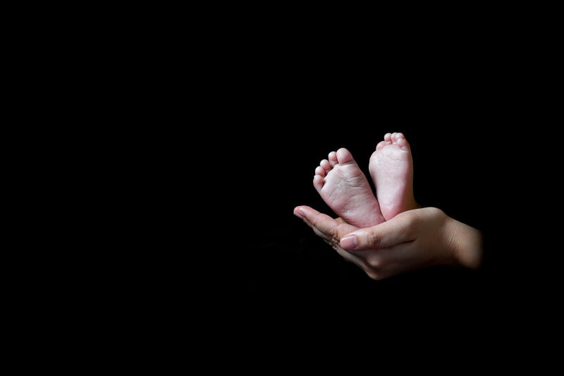 Cropped hands holding baby feet against black background