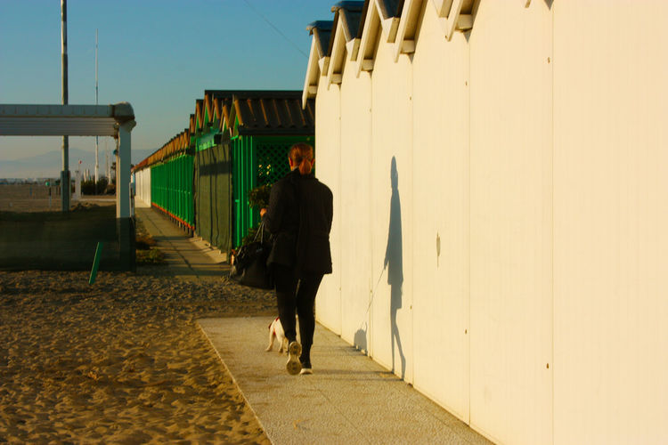 Rear view of man walking on footpath amidst buildings in city