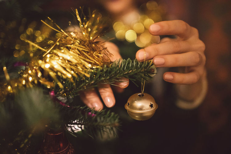 Cropped hands of woman tying decoration on christmas tree