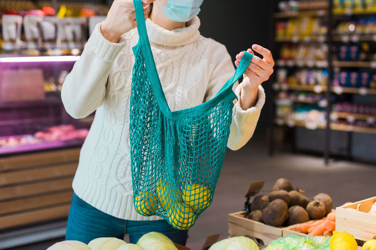 Midsection of woman holding mesh bag at supermarket