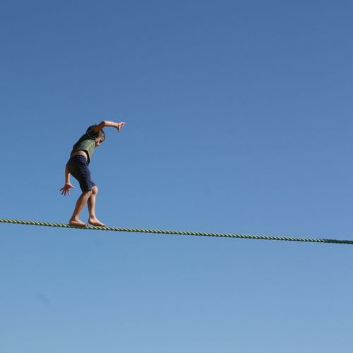 Low angle view of boy walking on tightrope against clear blue sky