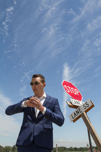 Low angle view of businessman looking away while standing by stop sign against sky