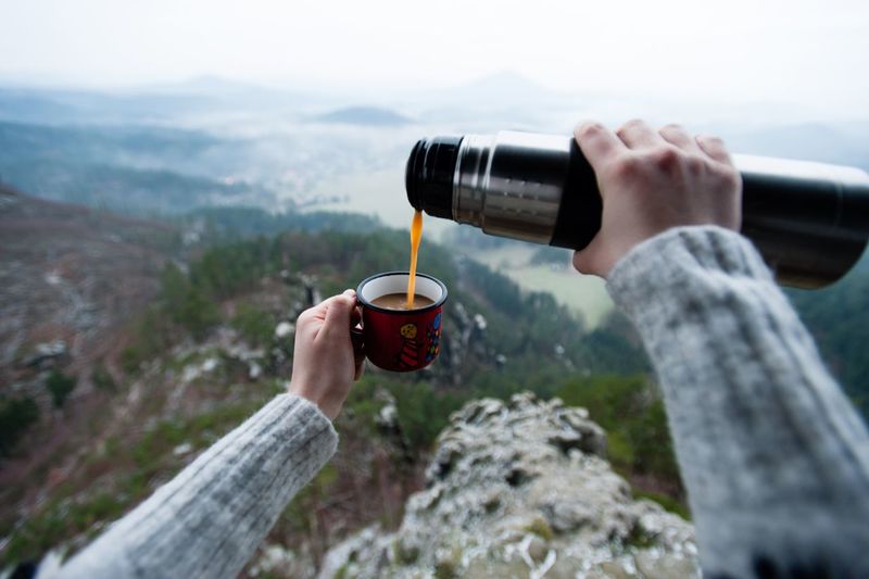 Cropped hands pouring coffee in cup against mountains
