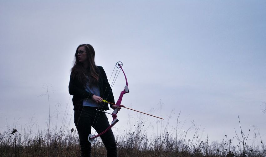 Woman practicing archery against sky