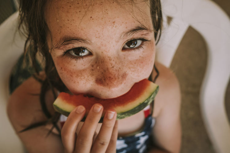 High angle portrait of wet girl eating watermelon while sitting on chair