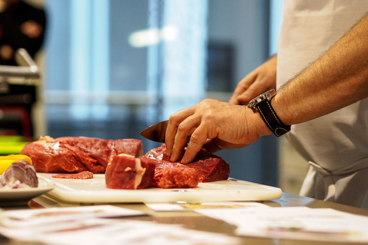 Midsection of chef cutting meat at table