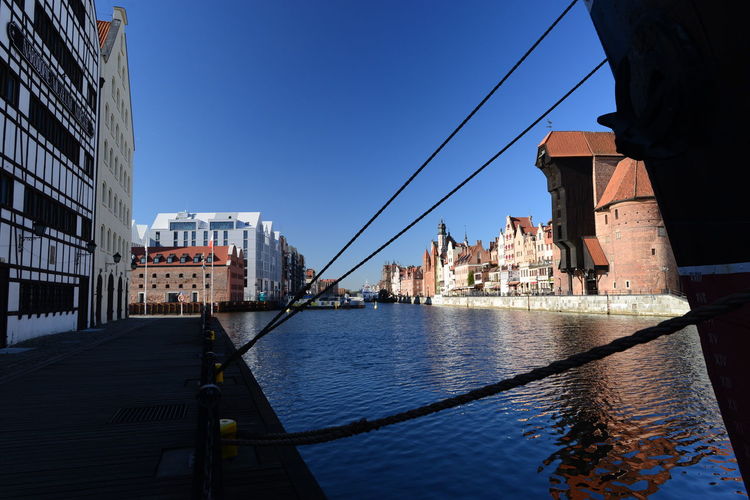Bridge over river by buildings in city against clear blue sky