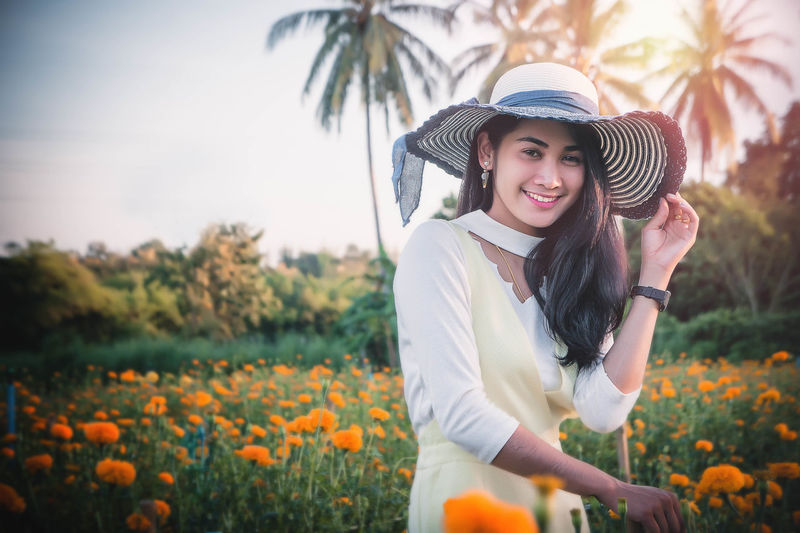 Portrait of smiling young woman wearing hat while standing in park