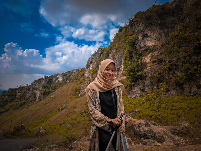 Smiling young woman standing on mountain against sky