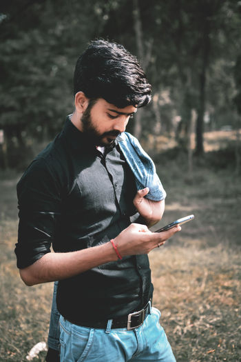 Young man using mobile phone while standing on grass