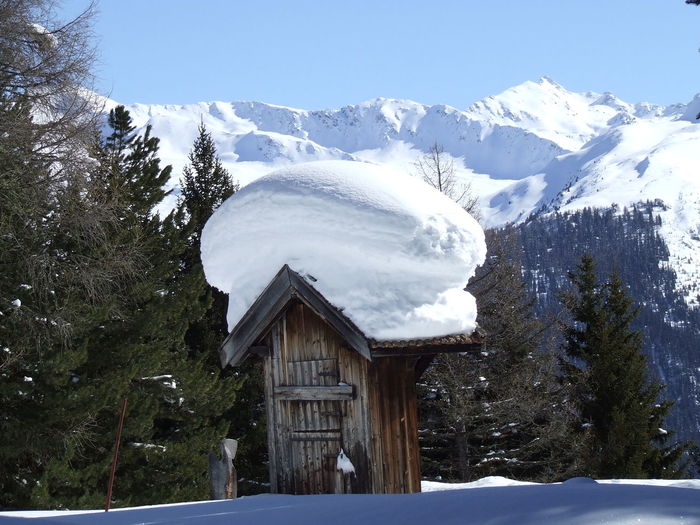 Snow covered hut on field against mountains 