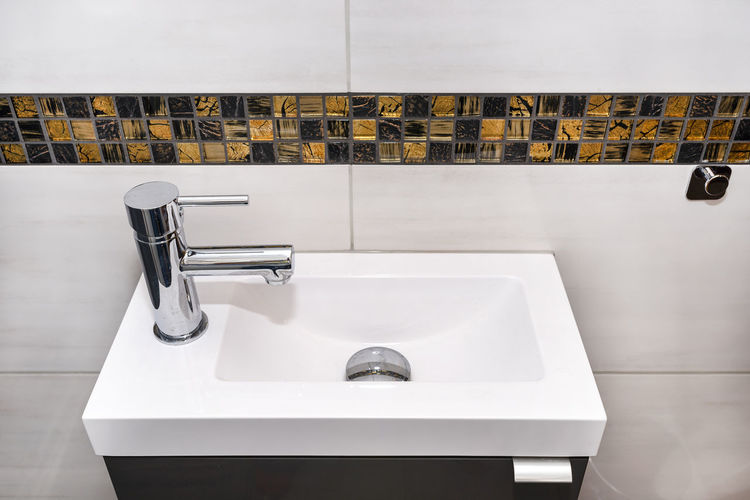 A small rectangular sink with a silver tap on the left in a tiled bathroom.