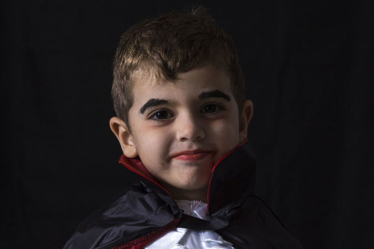 Close-up portrait of boy wearing costume against black background