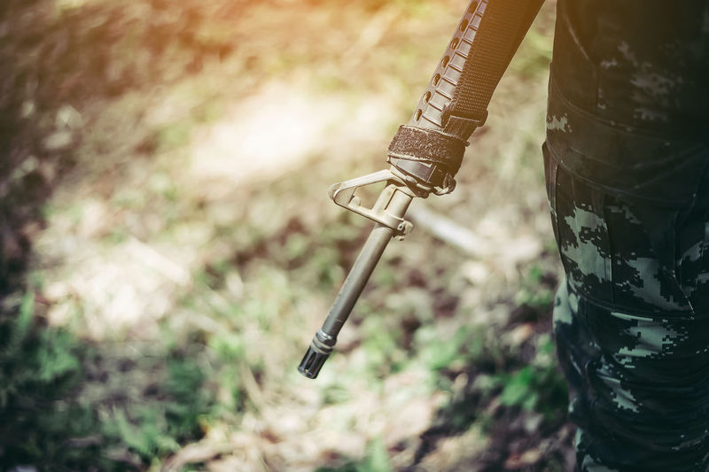 Midsection of military office holding weapon on field