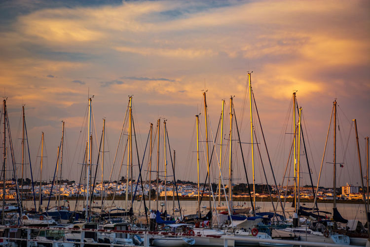 Sailboats moored at harbor against sky during sunset